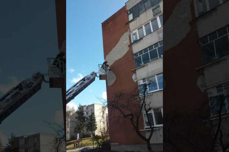 Tűzoltók távolítják el a meglazult vakolatot az erős szélben egy magas tömbházról