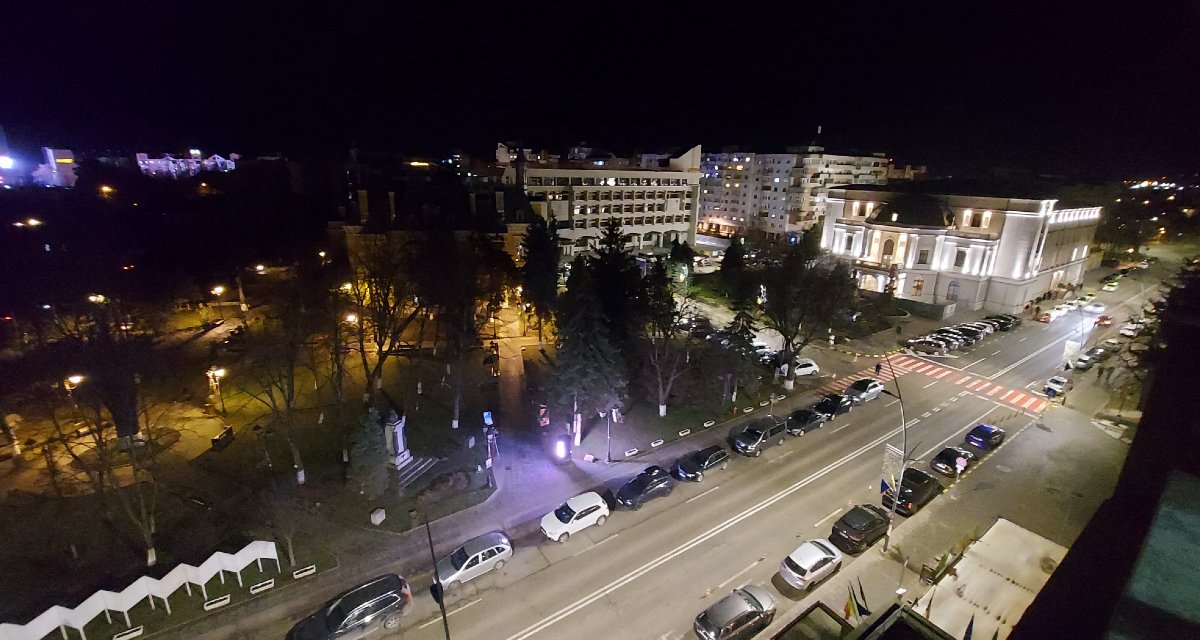 Botoșani by night. Elég jól látszik, hogy parkoló, az nincs. A kép jobb szélén a színház, épp előadás van. Középen, a homályba burkolózó épület a polgármesteri hivatal. 