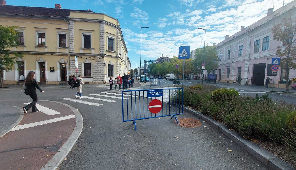 Ott a tiltótábla, mindkét irányból, a Petőfi és Egyetem utca kereszteződésében. Pedig be szabad hajtani. De nem! Az ellentmondás csimborasszója. És mit tesz a smekker autós? A kordon elé parkol. Néha öt autó is áll egymás mögött. Szép urbanisztikai megoldás!