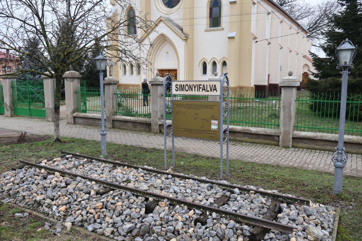 Vágányrészlet és felirat emlékeztet arra a római katolikus templom előtt, hogy hol állt a kisvasút egykori simonyifalvi végállomása &bullet;  Fotó: Pataky Lehel Zsolt