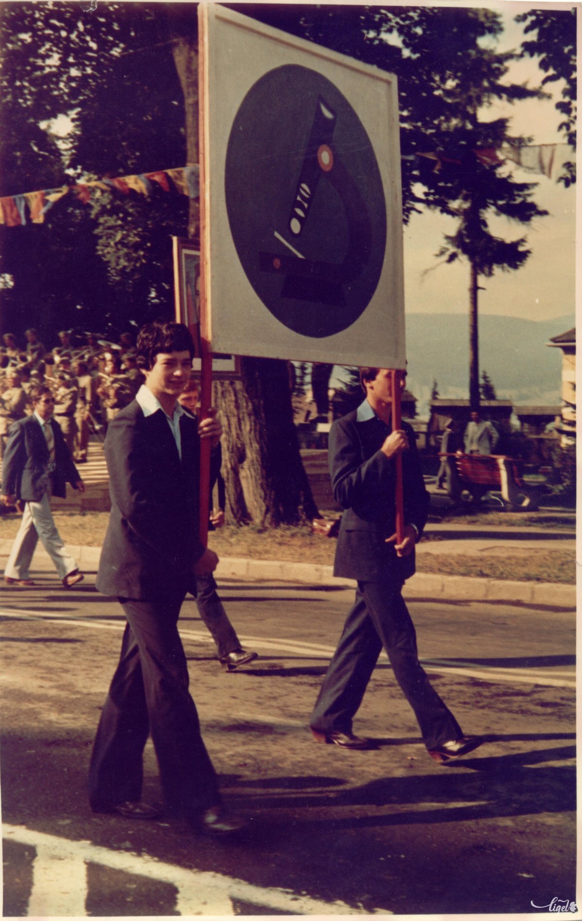 Gimnáziumi tanulók egy mikroszkópot ábrázoló táblával – felvonulás augusztus 23-án a mai Vár téren 1979-ben vagy 1980-ban. A fotó tulajdonosa: Nagy-Galaczi Géza. Fotó: Nagy-Galaczi György (A Csíki iskolák múltja című iskolatörténeti kiállítás anyagából) •  Fotó: Daczó Katalin gyűjtése